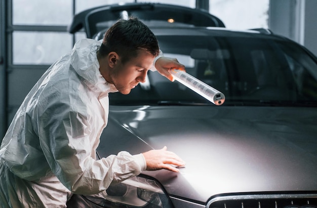 Zilverkleurige auto Man in uniform werkt in de autoservice