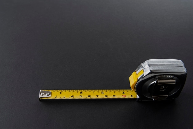 Zilverkleurige flexometer of meter met geel meetlint op een zwarte achtergrond