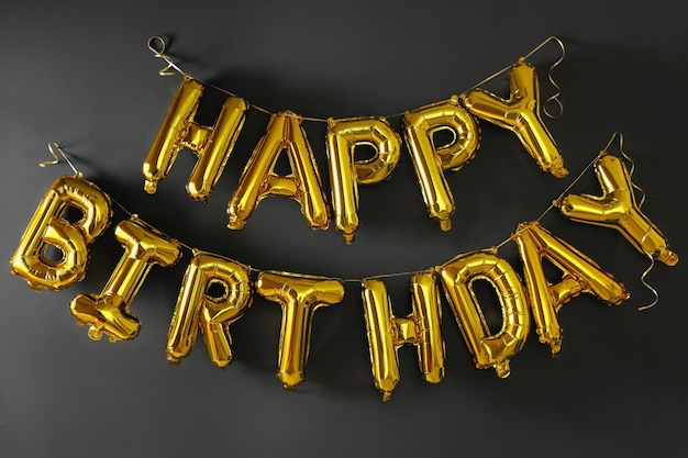 Foto zin happy birthday gemaakt van gouden ballonletters op zwarte muur