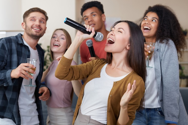 Zingende jonge mooie Aziatische vrouw die microfoon vasthoudt en zingt terwijl ze plezier heeft met