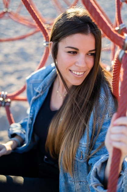Foto zinnige jonge vrouw die glimlacht terwijl ze midden op het touw op de speeltuin zit