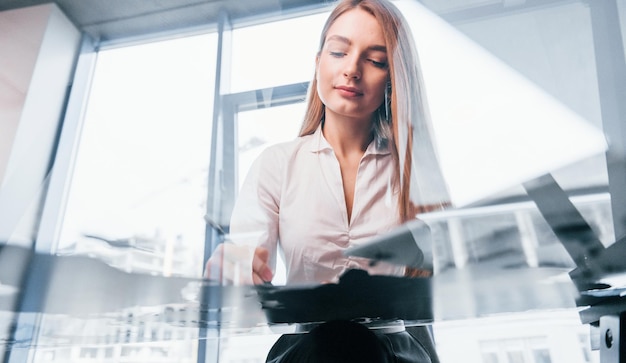 Zit bij de tafel Jonge vrouw in witte formele kleding is binnenshuis in het moderne kantoor