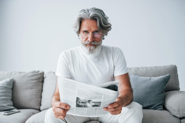 Zit op de bank Senior stijlvolle moderne man met grijs haar en baard binnenshuis