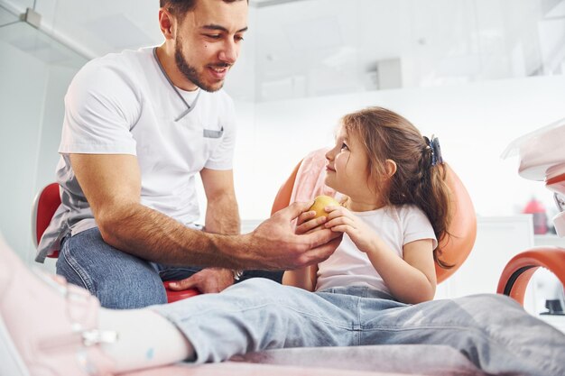 Zit op de stoel Klein meisje op bezoek bij tandarts in kliniek Conceptie van stomatologie