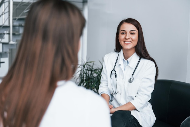 Zitten en praten Jonge vrouw heeft een bezoek aan een vrouwelijke arts in een moderne kliniek