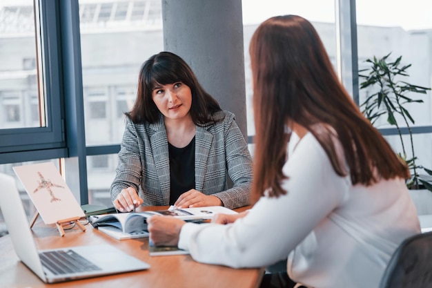 Zittend bij de tafel Twee vrouwen in formele kleding is binnen in het moderne kantoor werkt samen