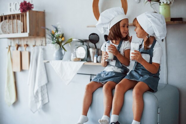 Zittend op de koelkast. Familie kinderen in witte chef-kok uniform eten eten in de keuken.