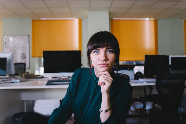 Zitting van de arbeiders de jonge mooie vrouw in een modern bureau en het bekijken de camera. office leven