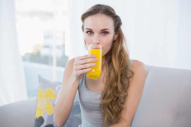 Zitting van de inhouds de jonge vrouw op bank het drinken glas jus d&#39;orange