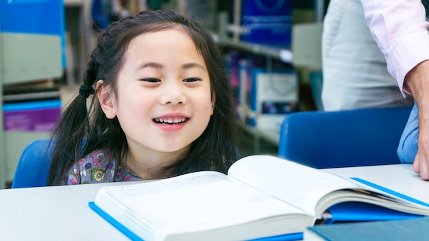 Zitting van het Smiley het Aziatische leuke meisje en het lezen van boek op de lijst