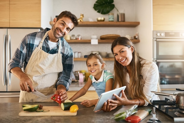 Zo brengen we onze zaterdagen door Portret van twee gelukkige ouders en hun jonge dochter die samen een nieuw recept proberen in de keuken