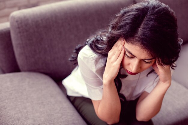 Zo verdrietig. Ongelukkige, ongezellige vrouw die haar slapen aanraakt terwijl ze zich erg van streek voelt