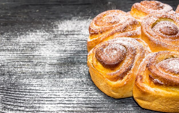 Zoet broodje met suikerpoeder op de zwarte houten tafel