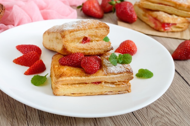 Zoet smakelijk bladerdeegdessert op een plaat op een houten achtergrond. Heerlijke huisgemaakte koekjes met aardbeienjam, bessen en suikerpoeder