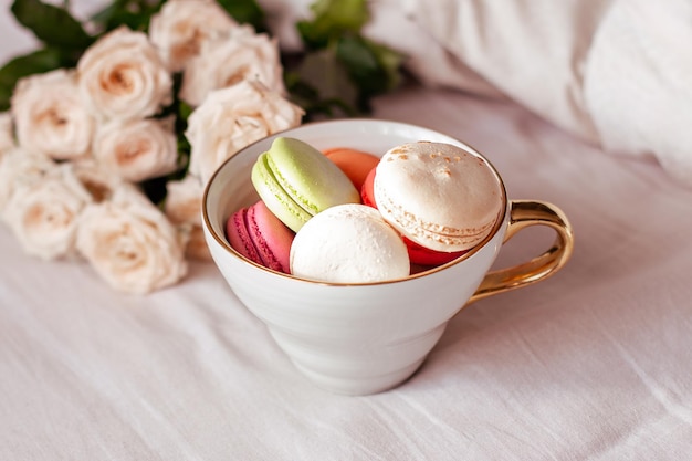 Zoete bitterkoekjes in mok en witte rozen