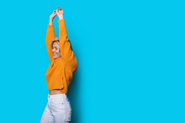 Zoete blanke vrouw poseren met handen omhoog op een blauwe achtergrond met lege ruimte