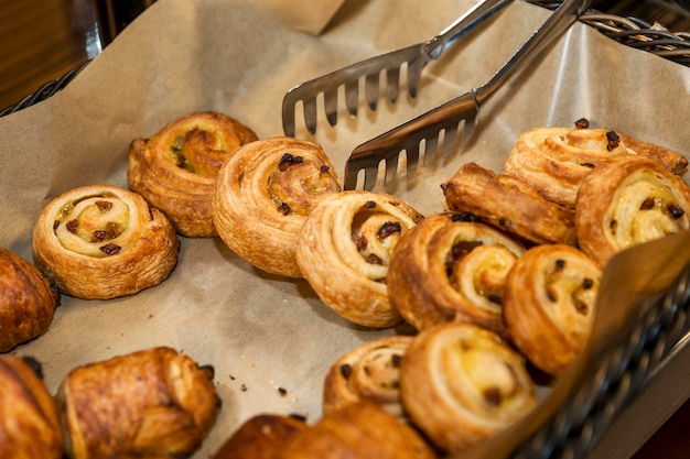 Zoete broodjes met metalen tang in een rieten mand op de buffettafel Catering voor vakanties en evenementen Close-up