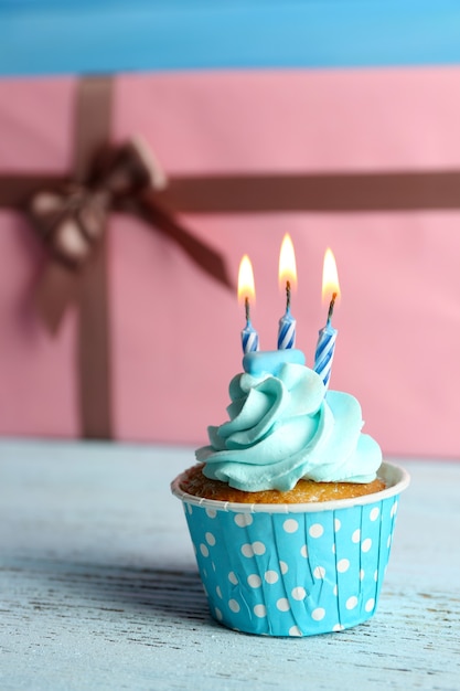 Zoete cupcake met kaars op blauwe houten tafel tegen roze huidige vakken