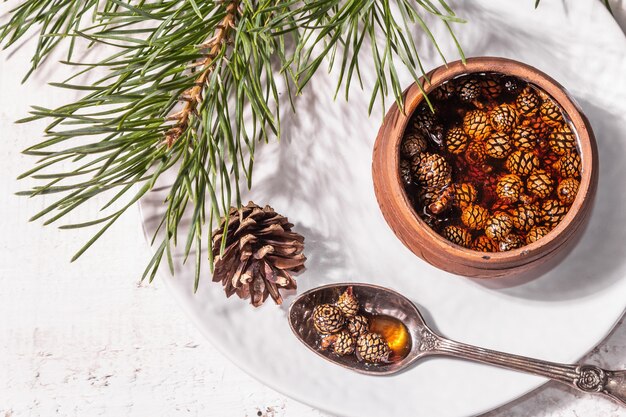 Zoete dennenappeljam. Traditioneel Siberisch dessert, verse groenblijvende takken. Trendy hard licht, donkere schaduw. Witte houten achtergrond, bovenaanzicht