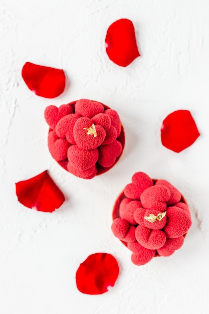 Zoete desserttartelettes met rode mousse-harten erop, versierd met rode rozenblaadjes, bovenaanzicht