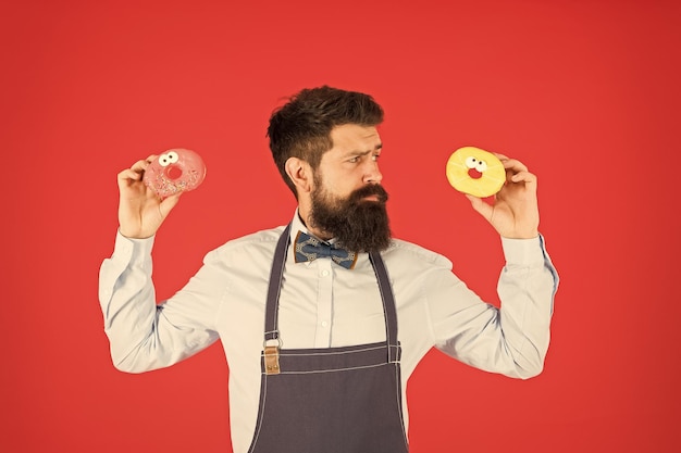 Zoete donut ober in café donut calorieën geglazuurde donut goed verzorgde man in schort die donuts verkoopt donuts voedsel gebakken goederen snoep en cakes junk food hipster baarde bakker houdt donuts