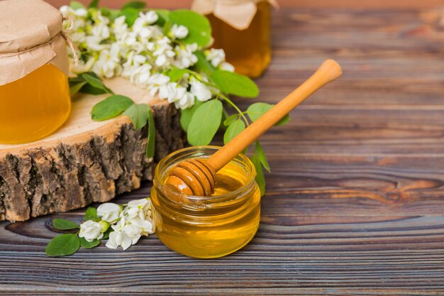 Zoete honingpot omgeven door lente acacia bloesems Honing stroomt van een lepel in een pot potten met heldere verse acaciahoning op houten achtergrond