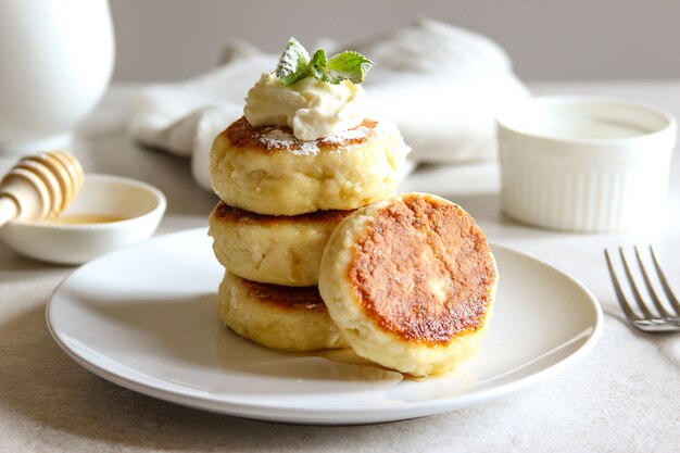 Zoete kaaspannenkoekjes met honing en room op een wit bord Huisgemaakte cheesecakes volgens recept