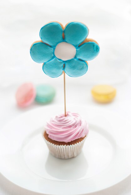 Zoete kleurrijke cupcake met koekjes in de vorm van een bloem op een witte plaat en macaroon op de achtergrond. hoog uitzicht. desserts voor een goed humeur bij de thee