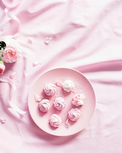 Zoete meringue op een roze bord Rozen in een witte vaas op een roze tafelkleed Plaats voor het label