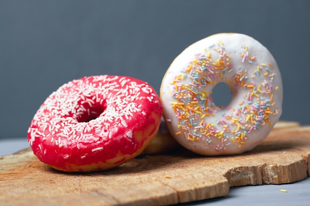 Zoete multi-coloured geassorteerde donuts met suikerglazuur en poeder op een houten raad op grijze achtergrond.
