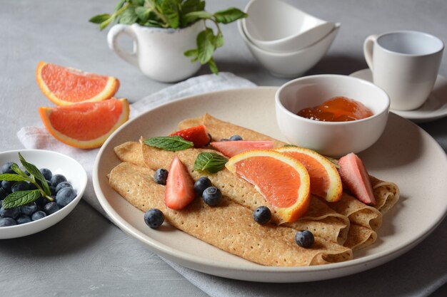 Zoete pannenkoeken omwikkeld met verse munt aardbeien bosbessen sinaasappels en jam