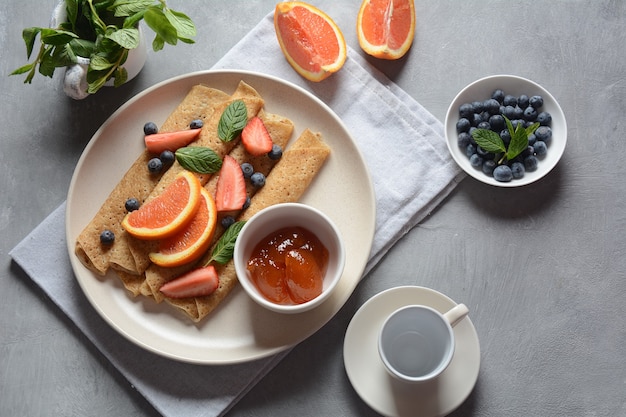 Zoete pannenkoeken omwikkeld met verse munt aardbeien bosbessen sinaasappels en jam