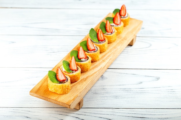 Zoete sushi roll met aardbei op houten plaat. Nieuwe trend in de Japanse cuisiune.