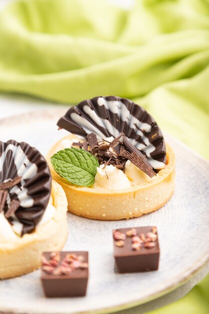 Zoete taartjes met chocolade en kaascrème met kopje koffie op een grijze betonnen achtergrond en groen textiel. Zijaanzicht, close-up, selectieve aandacht.