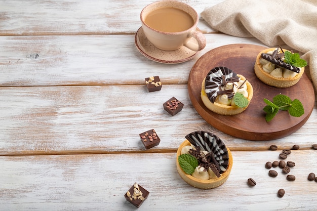 Zoete taartjes met chocolade en kaasroom met kopje koffie op een witte houten achtergrond en linnen textiel. zijaanzicht, kopieer ruimte.