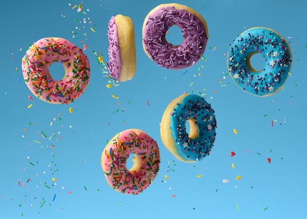 Zoete veelkleurige donuts zweven op een blauwe achtergrond, suikerhagelslag vliegen rond