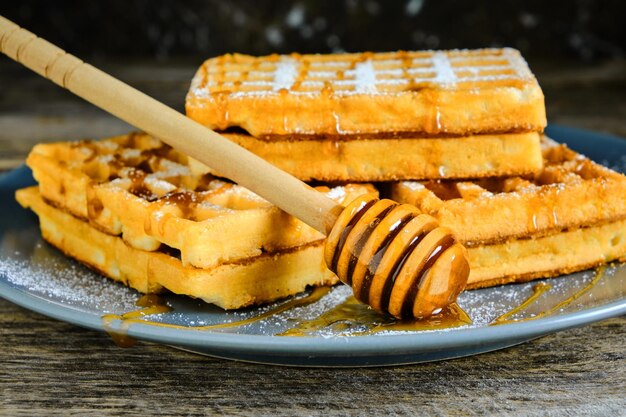 Zoete wafels besprenkeld met honing en bestrooid met poedersuiker op een blauw bord