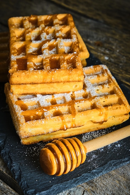 Zoete wafels besprenkeld met honing en bestrooid met poedersuiker op een leisteen