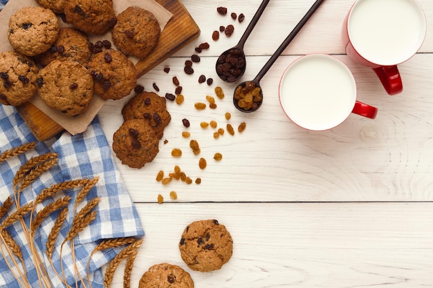 Zoete wintervakantie achtergrond met verschillende koekjes en kopje hete pittige melk op witte rustieke tafel met kopieerruimte. kersthaverkoekjes koken, bovenaanzicht. mockup voor recept