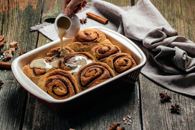 Zoete zelfgemaakte kaneelbroodjes. Vrouwenhand die vanilleroom verspreidt.