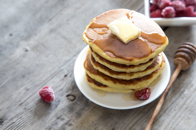 Zoete zelfgemaakte stapel pannenkoeken met boter, frambozen en honing voor het ontbijt