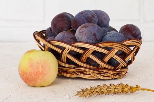 Zojuist rijpe pruimen geplukt in een rieten mand en een appel met een korenaar