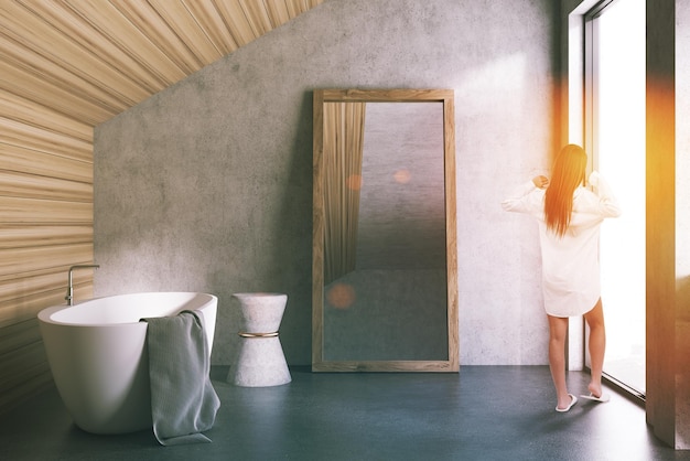 Zolder badkamer interieur met betonnen en houten wanden, een betonnen vloer, een badkuip en een grote spiegel op de vloer. Een vrouw 3D-rendering getinte afbeelding