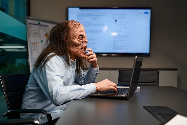 Zombie businessman working online on laptop computer in the office boardroom at night