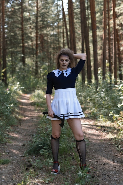 暗い森の中で斧を手にしたゾンビの女の子。ハロウィーンの衣装