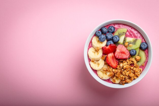 Zomer acai smoothie bowl met aardbeien, banaan, bosbessen, kiwi's en muesli op pastelroze achtergrond. Ontbijtkom met fruit en granen, close-up, bovenaanzicht, ruimte voor tekst