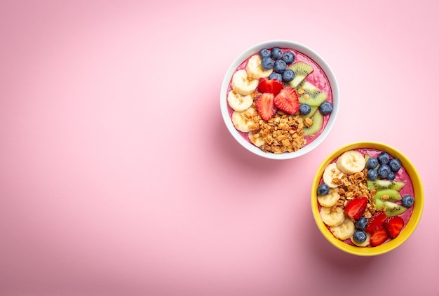 Zomer acai smoothie bowl met aardbeien, banaan, bosbessen, kiwi's en muesli op pastelroze achtergrond. Ontbijtkom met fruit en granen, close-up, bovenaanzicht, ruimte voor tekst