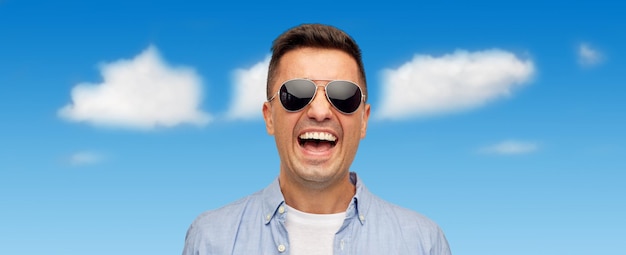 zomer, accessoires, stijl en mensen concept - gezicht van lachende Latijns-man van middelbare leeftijd in shirt en zonnebril over blauwe lucht en wolken achtergrond