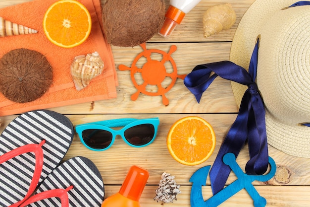 Zomer accessoires. Strand accessoires. Hoed, zonnebrandcrème, zonnebril, slippers en een sinaasappel op een natuurlijke houten tafel. bovenaanzicht.