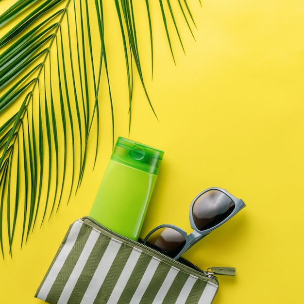 Zomer achtergrond. Samenstelling gestreepte cosmetische strandtas met sunblock en zonnebril op een gele achtergrond. Zomervakantie concept, zonnebrandcrème cosmetica en accessoires. Bovenaanzicht. Kopieer ruimte.